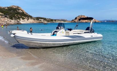 Spiaggia tra Maddalena e Caprera con persone che si rilassano e si bagnano, e un gommone De Luxe ormeggiato vicino alla riva | Fabatour Sardegna