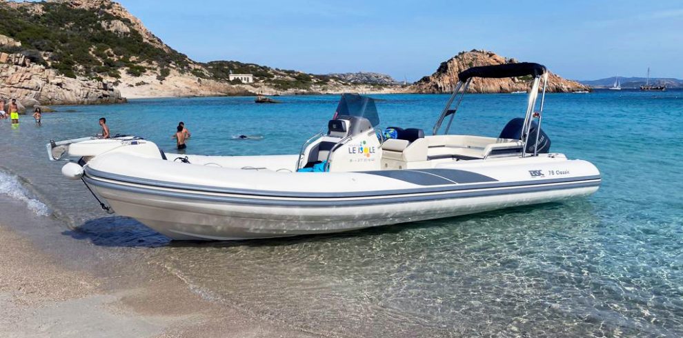 Spiaggia tra Maddalena e Caprera con persone che si rilassano e si bagnano, e un gommone De Luxe ormeggiato vicino alla riva | Fabatour Sardegna