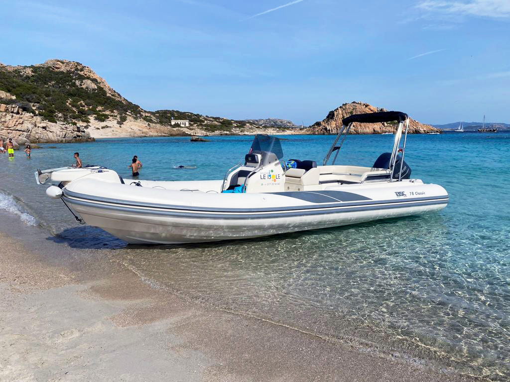 Spiaggia tra Maddalena e Caprera con persone che si rilassano e si bagnano, e un gommone De Luxe ormeggiato vicino alla riva | Fabatour Sardegna
