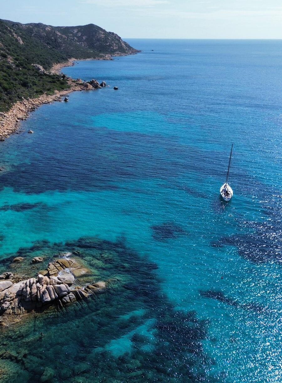 Barca a vela davanti alla costa rocciosa di Tavolara con acque turchesi e scogli levigati dal mare