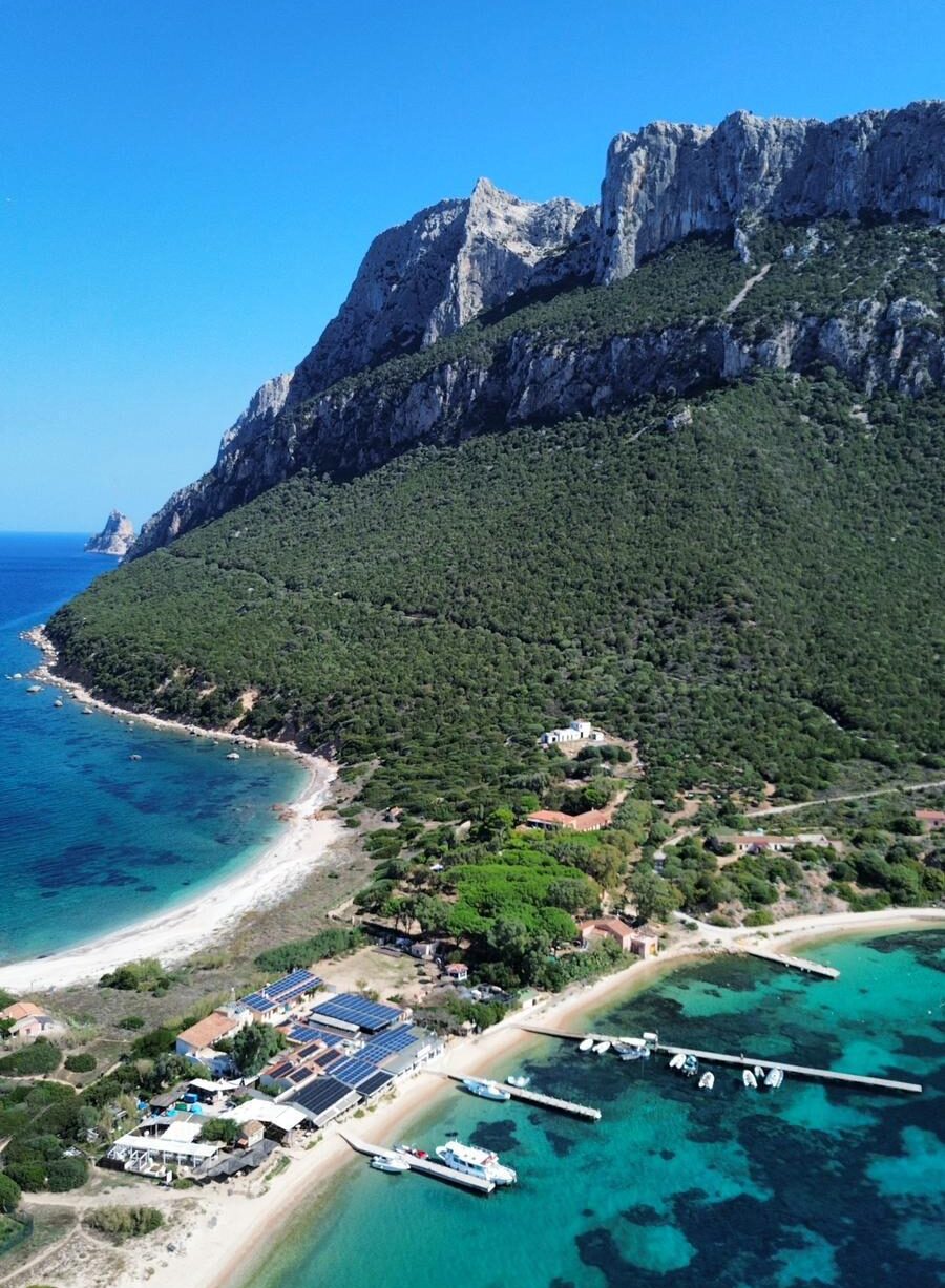Vista aerea della spiaggia e del pontile dell’Isola di Tavolara con la maestosa montagna sullo sfondo