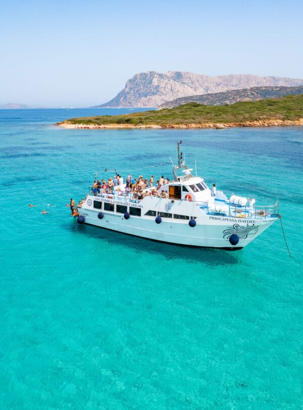 The motorboat Principessa Haydée anchored near Tavolara Island with passengers enjoying a swim in turquoise waters during the mini cruise.